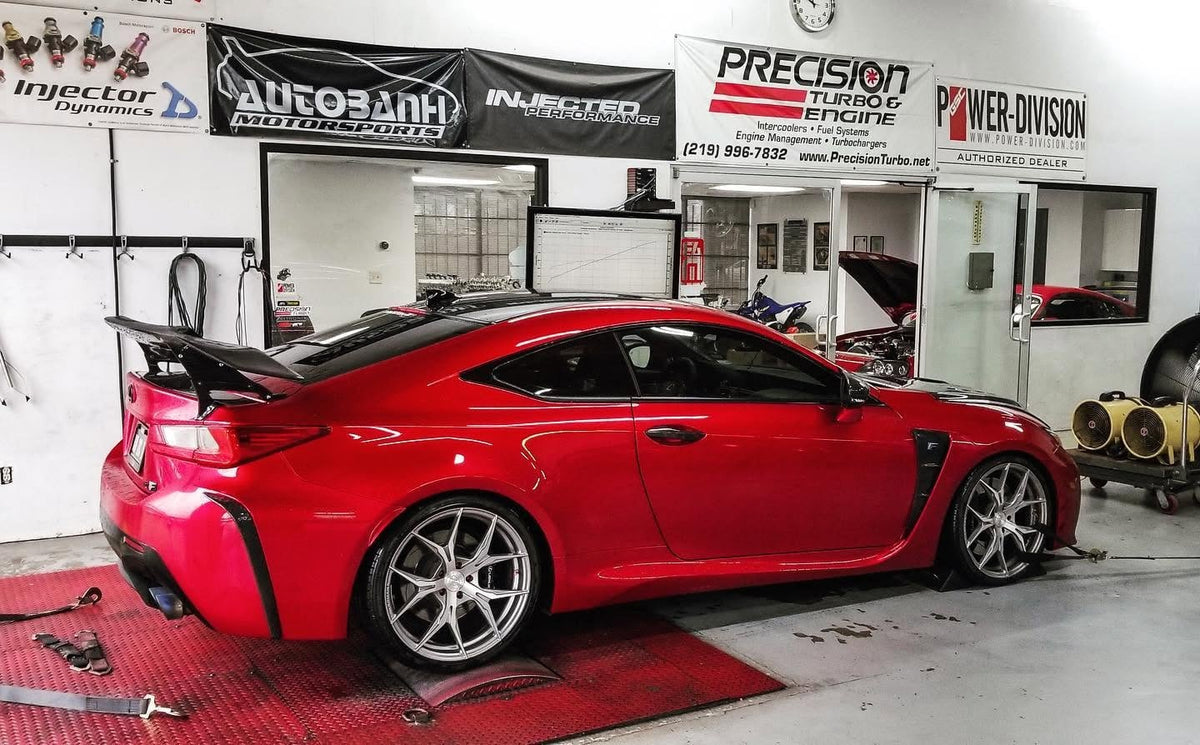 Red Lexus RC F secured on a workshop dynamometer with its hood open.